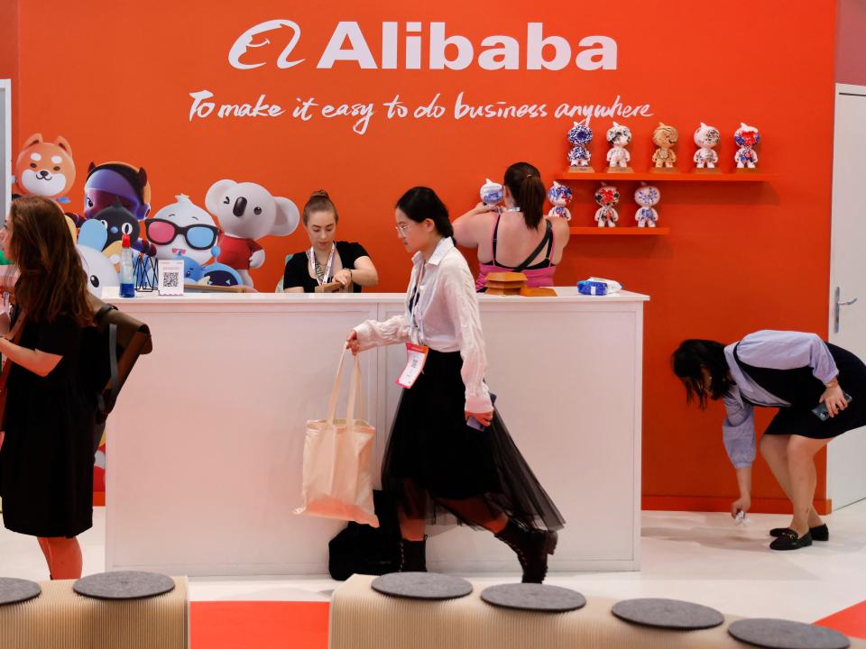 People walk past the Alibaba logo on an orange wall.