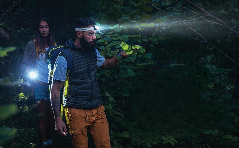 One person with a flashlight, one with a headlamp in the woods at night