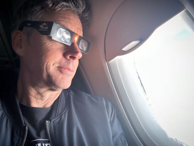 GeekWire reporter Kurt Schlosser tests his eclipse glasses as his flight from Seattle to New York City passes over the Great Lakes on Friday. (GeekWire Photo / Kurt Schlosser)
