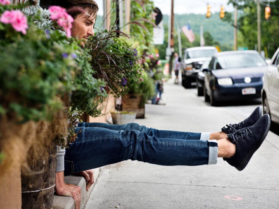 A man sitting on a flower-lined sidewalk with his legs out to show off his Allbirds wool runners.