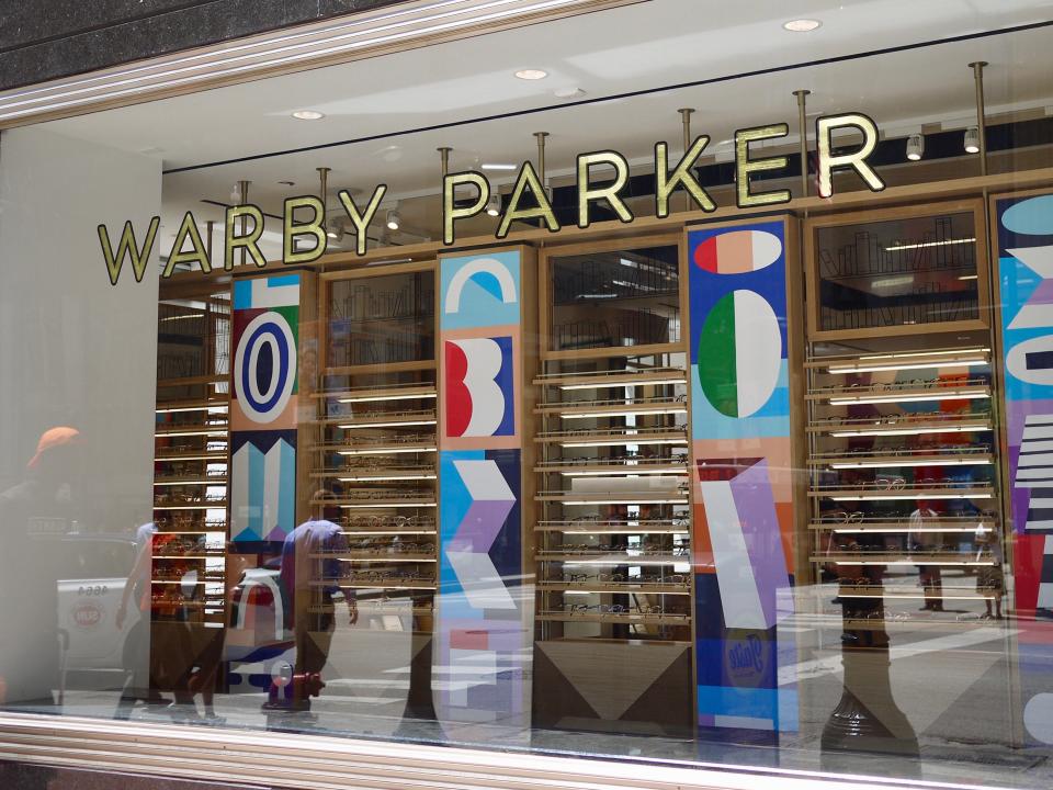 A street window looking into a Warby Parker store with artistic patterns on the walls.