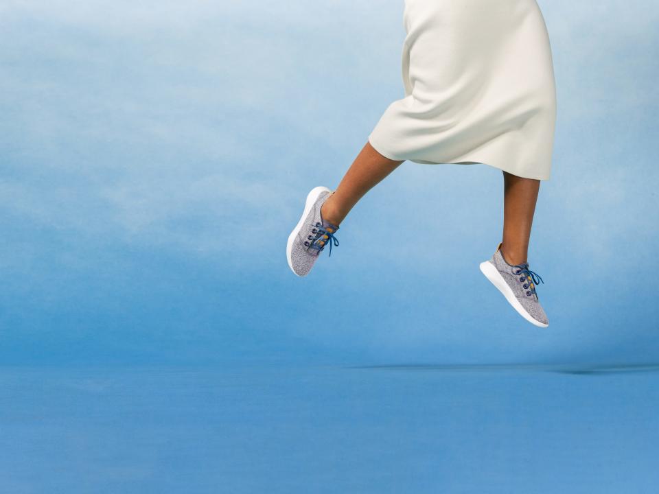 A model in a white gown jumping out of frame to reveal a grey pair of SuperLight sneakers.