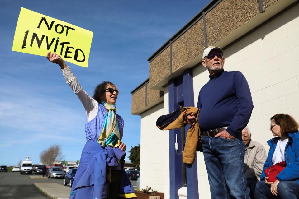Solano County and Rio Vista residents Kathleen Threlfall, left, and Bill Mortimore protest outside a press conference with a sign reading "Not Invited"